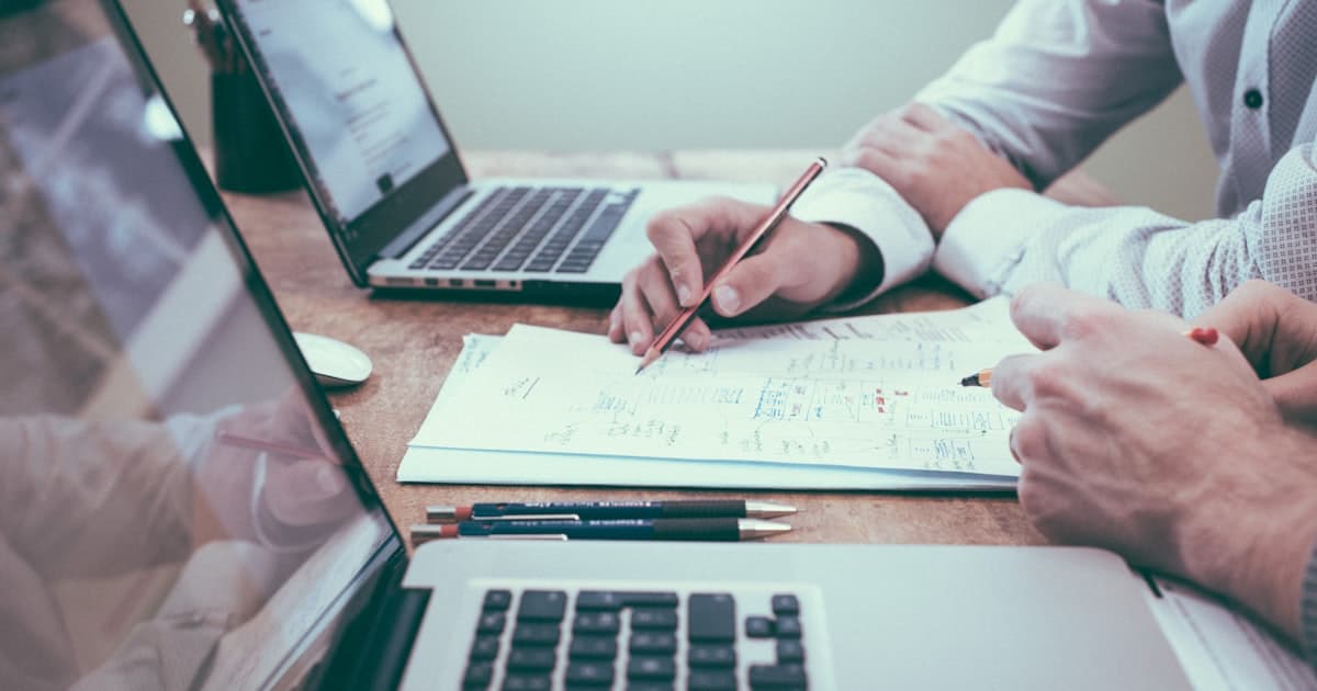 Dos personas revisando números y papeles de administración en un escritorio